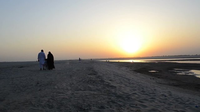 Muslim family with kid walking on sand during evening