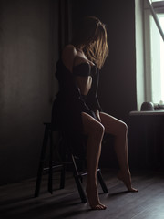 Seductive, beautiful and attractive young woman with loose brown hair, sexy shapely figure and long legs in the black seamless underwear and wool coat is posing on the chair in the studio