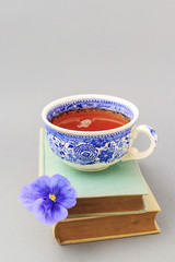 Cup of tea, stack of books and single pansy flower.