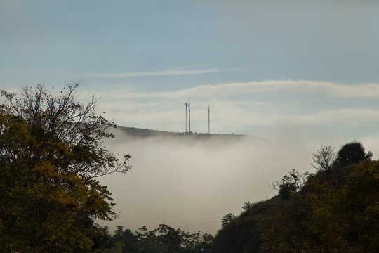 Fototapeta Montaña con niebla / Montaña cubierta de niebla con dos antenas de telefonía en la cima
