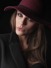 Portrait of an elegant and attractive young woman in the black wool coat, seamless underwear and marsala broad-brim hat on her head, studio photoshoot
