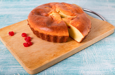 Home-made pie and several red berries nearby. Pie lies on a wooden board, a blue table in rural style. From pie the piece is cut off.