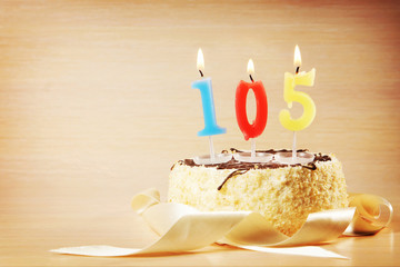 Birthday cake with burning candle as a number one hundred and five. Focus on the candle