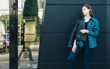 Portrait of brunette girl wearing leather jacket standing outdoors in the city against the black urban wall