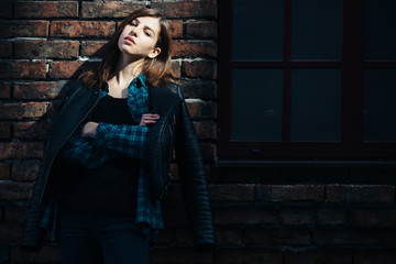 Lifestyle fashion portrait of brunette girl in rock black style, standing outdoors in the city street