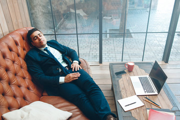 Tired office worker with eyes closed lying on leather sofa. Working day, fatigue and daily routine concept.