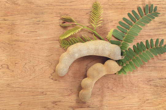 Sweet ripe tamarind pods with leaflets on old wood background