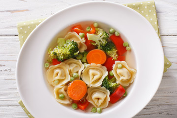 Italian soup with tortellini and vegetables closeup at the plate. horizontal top view