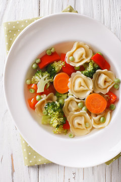 Italian tortellini soup with broccoli, peas, carrot and pepper close-up. vertical top view
