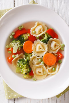 Italian soup with tortellini and vegetables closeup at the plate. vertical top view
