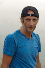 Happy Young Bearded Man sitting on view point with a seascape wearing in blank blue t-shirt and black Cap