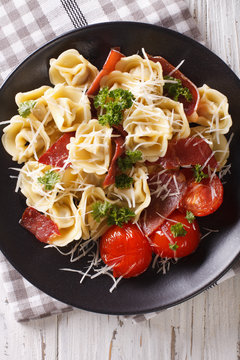 Freshly cooked tortellini with prosciutto and parmesan on a plate. Vertical top view