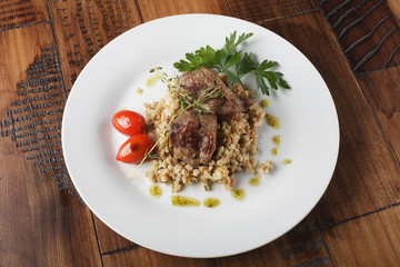 Veal (beef) cheeks with pearl barley porridge and greens in a white plate. Wooden background.