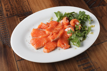 Smoked trout with greens on a white plate. Wooden background.