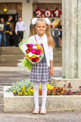 Fototapeta premium Grower Baby girl first-grader with a bouquet of flowers at the school