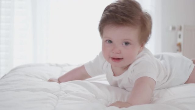 Cute happy baby cuddling on a soft blanket while lying on his tummy.
