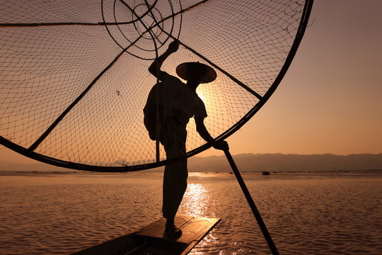 Burmese fisherman on bamboo boat catching fish in traditional way with handmade net. Inle lake, Myanmar (Burma) 