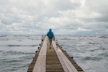 man walking on wooden pier on the background of stormy sea