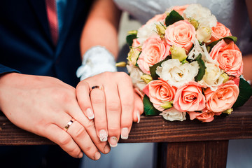 newlyweds hands with rings and a bouquet background