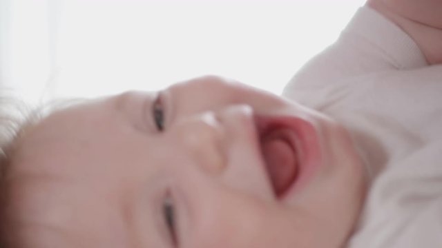 Close-up tracking shot of a mother's hand gently playing with her happy baby making him laugh.
