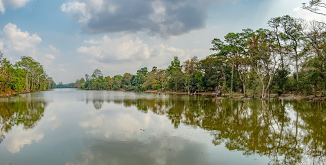Fototapeta premium Beautiful lake nestled among rainforest in Cambodia under blue sky with white clouds. It surrounding mysterious ruins of Angkor Thom in Siem Reap, Cambodia.