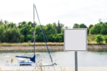 Square blank sign against small moored sailboat