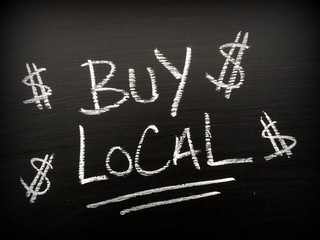 The words Buy Local written in white chalk on a blackboard with dollar signs as a reminder to support your local business