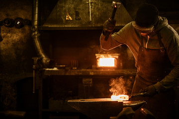 Blacksmith with brush handles the molten metal on the anvil in smithy