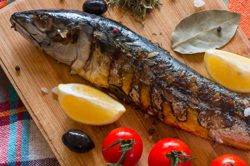 Mackerel fish on a wooden board with tomatoes and herbs
