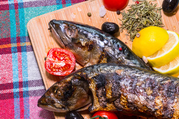 Mackerel fish on a wooden board with tomatoes and herbs