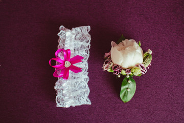 White garter and delicate boutonniere lie on violet background