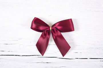 Brilliant red bow - a Christmas ornament. Red ribbon gift bow isolated on white wooden  background