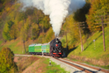 Old steam train on the mountain railway, surrounded by forest, tilt shift