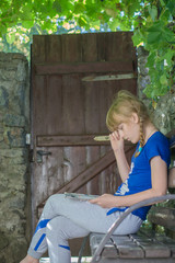 young teenage girl sit on bench at backyard under the thickets of grapes and reed journal book with...