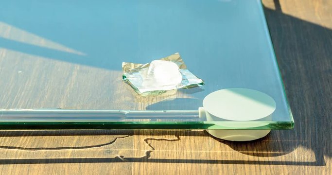 Ice cube melt on glass surface time lapse. A ray of sunlight heats an ice cube on a glass pedestal