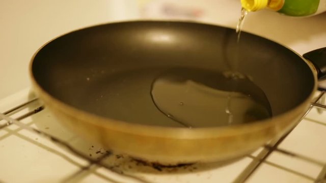 Mani di una donna che sta versando olio di girasole in una padella antiaderente prima della cottura delle crocchette di patate. 