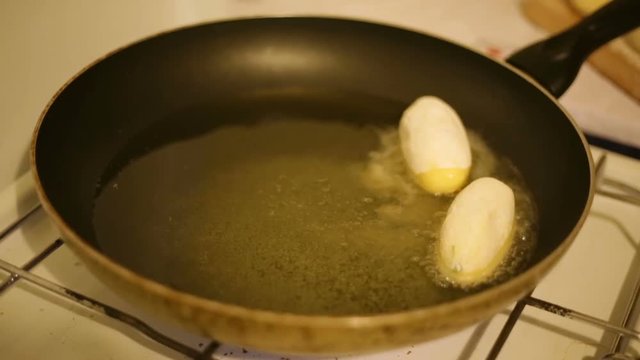 Crocchette di patate ripiene con prosciutto e provola che friggono in padella. 
