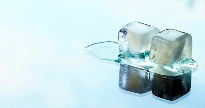 Two ice cubes melting on the glass surface on a background of running clouds. Time lapse