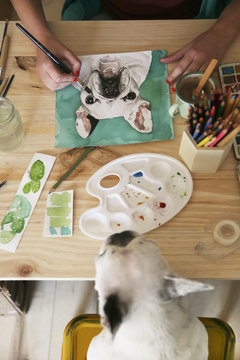Woman's hand painting an aquarelle of French bulldog