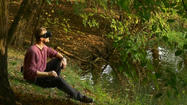Man in 360Vr Glasses Watching Video 360 Degrees Feels Real Turning His Head Playing Virtual Games in Sunny Day Park by Lake Then Removes the Headset