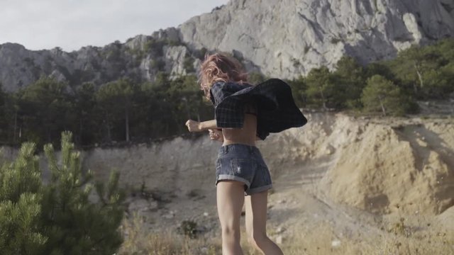 Skinny girl dancing and laughing while standing on the parapet in front of the rocks