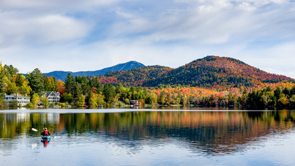 A panoramic view of Mirror Lake in Lake Placid, New York, on a sunny autumn day with colorful fall foliage on the mountains in the background