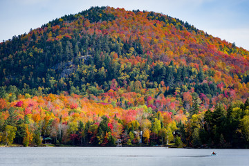 Obraz premium A closeup of a mountain with colorful autumn foliage across Mirror Lake in Lake Placid on a sunny fall day