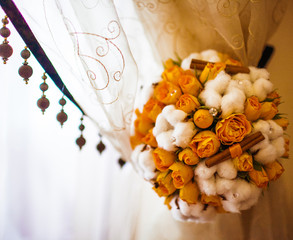 Wedding bouquet made of orange roses and white cotton hangs from
