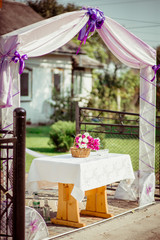 Pink flowers stand under the fence decorated with violet cloth
