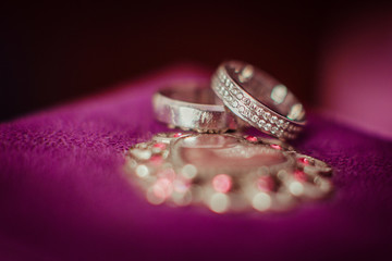 Silver wedding rings lie over the violet pillow