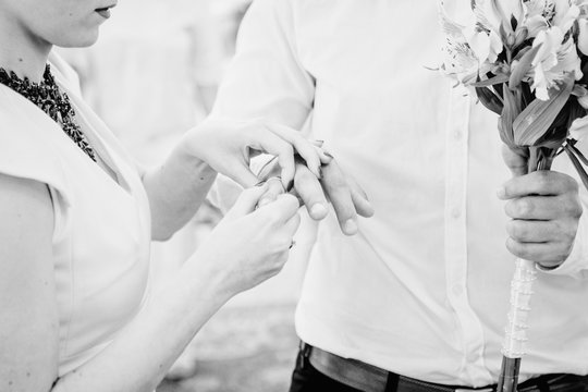 Black and white picture of bride adjusting a ring on groom's fin