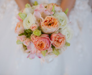 Bride holds in her hands a bouquet of peach peonies