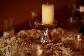 White candle stands on the sprakling holder in the middle of a w