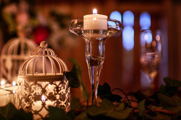 White candle in a little glass vase stands on the green garland